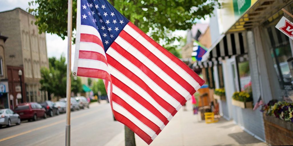 An American flag in focus in front of a busy street.