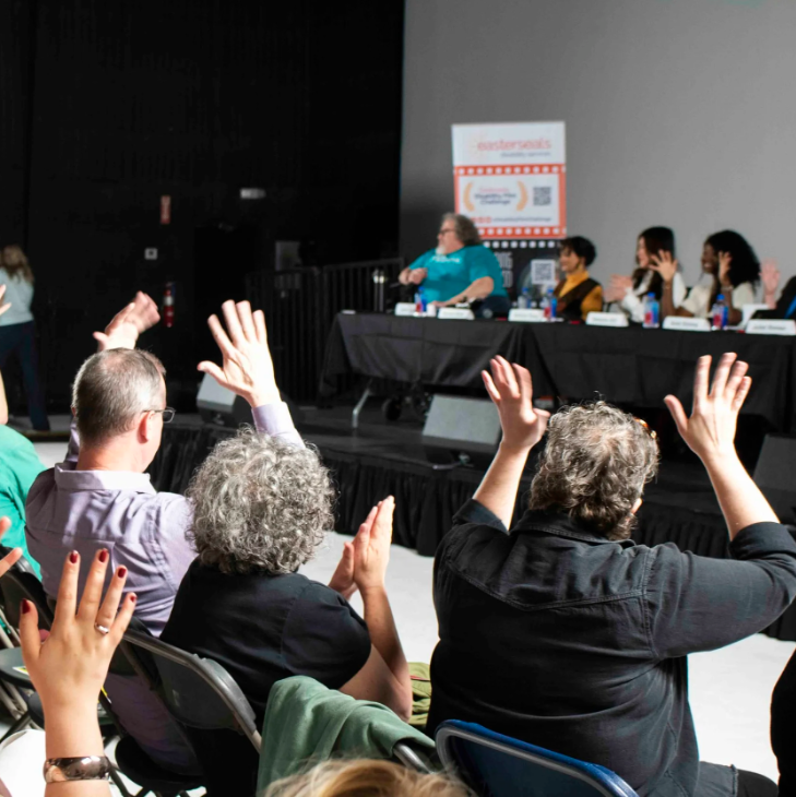 An audience waving their hands in applause for a panel of presenters